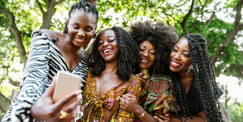 Four Black women laughing and taking a selfie photo