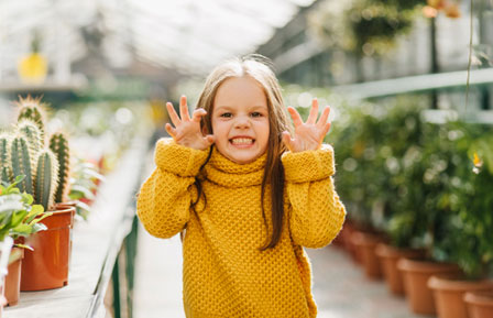 a smiling child in a yellow sweater playfully makes a claw gesture with hands raised
