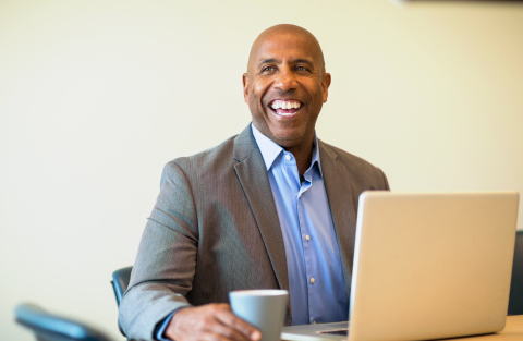A middle-aged Black man laughs while working on a computer