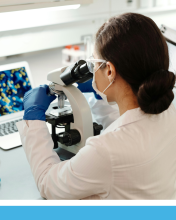 A woman in a lab coat looks into a microscope.